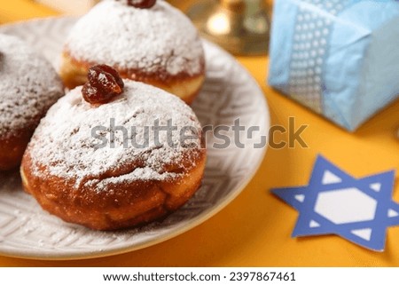 Plate with donuts and gift box for Hanukkah celebration on yellow background