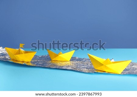 Yellow origami boats with foil on color background