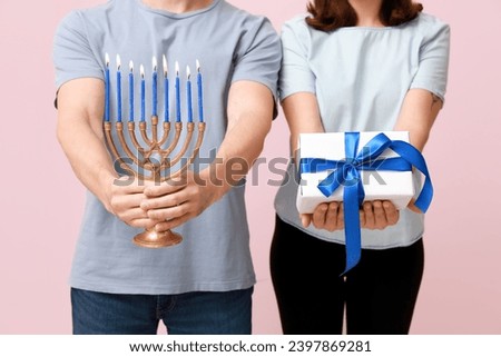 Lovely couple with menorah and gift box on pink background, closeup. Hanukkah celebration