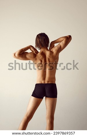Shirtless young man with fit body standing in underwear against grey studio background. Relief strong healthy back, spine. Concept of men's beauty, health, body care, sportive lifestyle Royalty-Free Stock Photo #2397869357