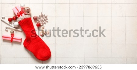 Beautiful Christmas sock with gifts and decorations on light tile background with space for text
