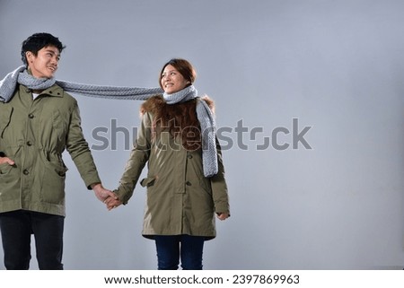 Young happy couple in green coat with scarf standing posing isolated over gray background