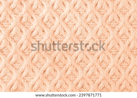 Demonstrating the colors of 2024 - Peach Fuzz. Knitted peach background. Large knitted fabric with a pattern. Close-up of a knitted blanket.