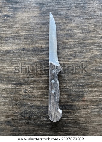 interior top view photo of a silver metal pointy knife with a wood wooden handleon a wood work top background table
