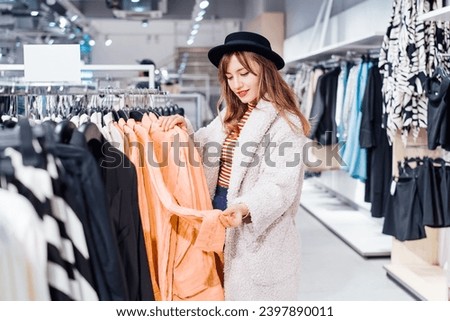 Fashion woman customer looking on peach color shirt in store. Buying clothes using fitting concept while choosing, professional stylist creating trendy look according to color of the 2024 year. Royalty-Free Stock Photo #2397890011