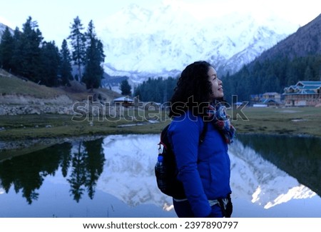 Asian female tourist having a picture taken with a view of the snow capped Nanga Parbat mountain and its reflection in the pond on Fairy Meadows - a popular destination in Pakistan.