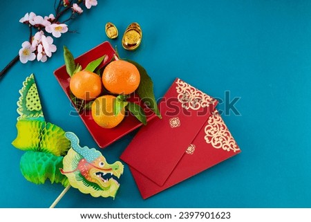 Chinese New Year of Green Dragon. Red packet envelope, flowers, mandarins, festival decorations on teal color background. Flat lay, top view.