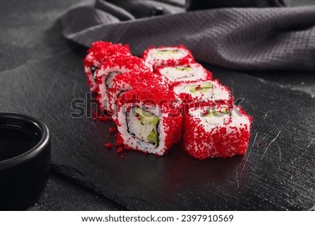 Vibrant California roll filled with crab and avocado, topped with bright red tobiko, served on a sleek black slate.