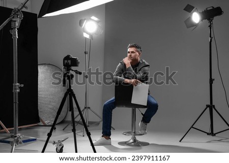 Casting call. Man with script sitting on chair and performing in front of camera in studio Royalty-Free Stock Photo #2397911167