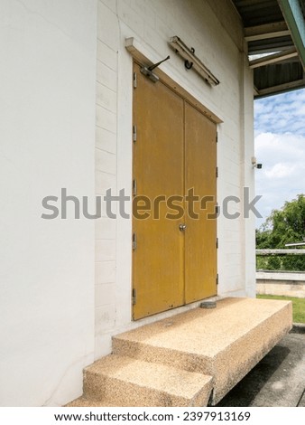 The yellow metal door with the door closes on the white concrete wall to the control room of the water filter plant, front view with the copy space.