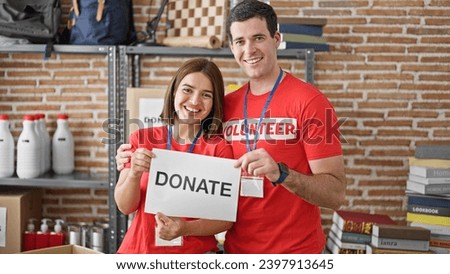 Man and woman volunteers standing together holding paper with donate message at charity center