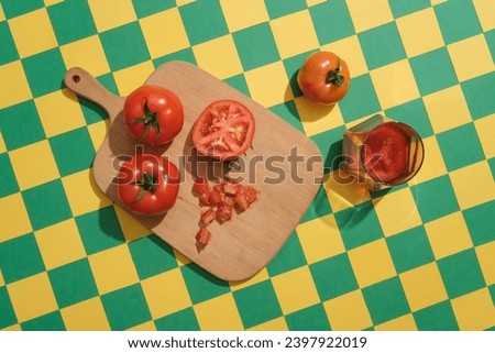 On the green and yellow checkered background, a wooden cutting board container fresh red ripe tomatoes decorated with a glass of tomato juice. Creative background for advertising