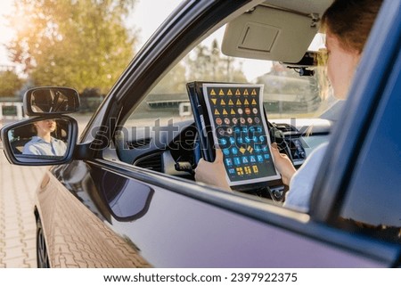 Young girl learns road signs while sitting in a car passing the driving test. Driving school novice driver concept. Royalty-Free Stock Photo #2397922375