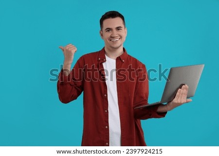 Special promotion. Happy young man with laptop pointing at something on light blue background, space for text