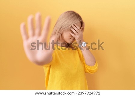Young caucasian woman wearing yellow sweater covering eyes with hands and doing stop gesture with sad and fear expression. embarrassed and negative concept. 