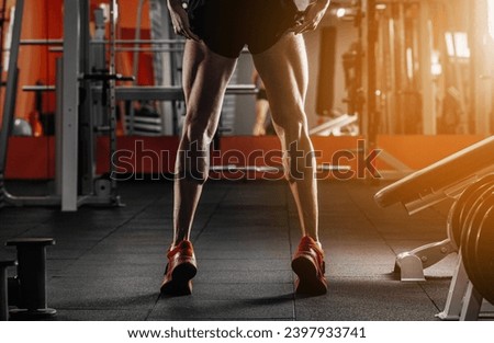 Trained legs with muscular calves in sneakers in fitness training gym Toned image Royalty-Free Stock Photo #2397933741