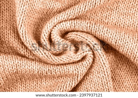 Demonstrating the colors of 2024 - Peach Fuzz. Knitted peach background. Large knitted fabric with a pattern. Close-up of a knitted blanket.
