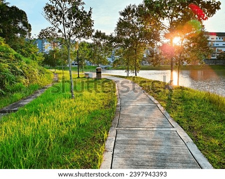 Beautiful park at sunny day UiTM Puncak Alam, Selangor. Small concrete walkway on green grass lawn in park with warm sunset sunlight. Outdoor city park landscape photography.