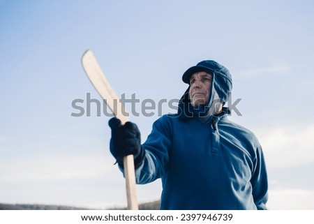 Portrait of an elderly man with a hockey stick against the background of the sky.