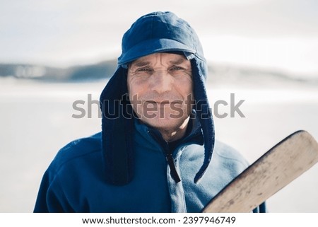 Elderly man with a hockey stick on a frozen lake in winter. Looking into the camera.