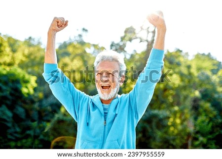 Smiling active senior man jogging exercising and having fun and celebrating success rasing hands taking a break in the park, concept of competition, winning, victory and strength Royalty-Free Stock Photo #2397955559