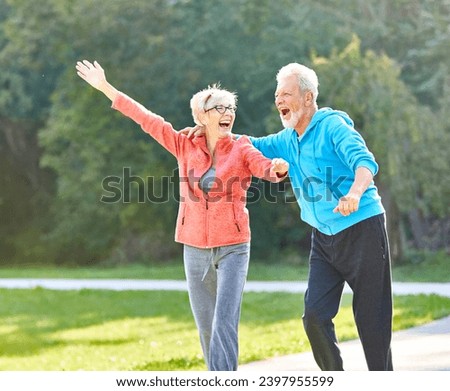 Smiling active senior couple jogging exercising and having fun and celebrating success rasing hands together taking a break in the park Royalty-Free Stock Photo #2397955599