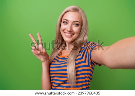 Selfie of attractive young blogger girl greetings with auditory in social media live stream show v sign isolated on green color background