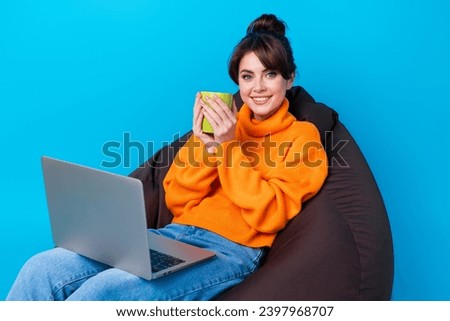 Photo of pretty shiny lady wear knitted pullover sitting bean bag drinking tea working modern gadget isolated blue color background