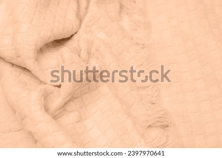 Background with color of the year -2024. Trendy color peach fuzz. Textured background for design. Knitted fabric with a checkered pattern, top view