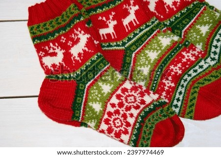 Beautiful Christmas socks with patterns of reindeer, fir trees, snowflakes and flowers, hand knitted from red, green and white wool yarn on a background of white painted boards. Handmade.