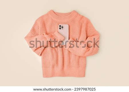 Knitted orange sweater with smartphone. Peach Fuzz - color of the year 2024. Women's warm jumper, stylish autumn or winter clothes. Fashion autumnal outfit. Color trend. 