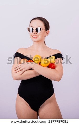 Smiling cool girl in sun glasses in black swimsuit posing with fruits and laughing.