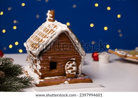 Christmas house made of gingerbread cookies decorated with sugar icing on blue background with bokeh garland
