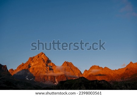 Scenic sunrise view of  mountain summit Monte Viso (Monviso) in the Cottian Alps, Piemonte, Italy, Europe. The rock walls of the Stone king are shining in warm red orange colors. Majestic landscape Royalty-Free Stock Photo #2398003561