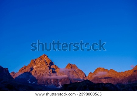 Scenic sunrise view of  mountain summit Monte Viso (Monviso) in the Cottian Alps, Piemonte, Italy, Europe. The rock walls of the Stone king are shining in warm red orange colors. Majestic landscape Royalty-Free Stock Photo #2398003565