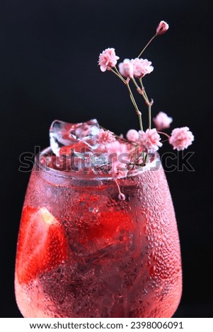 A delicious refreshing pink drink with strawberry slices and flowers. Ice cubes in the drink. Macro photo.