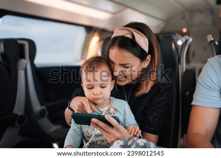 A happy mother shows baby application on mobil to her child as they sit together on the train
