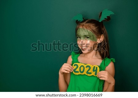 A laughing girl with a made-up face in the shape of a dragon shows the numbers of the 2024 new year. A child in the background with a copy space