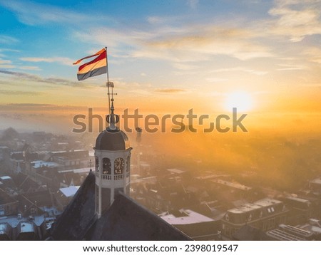Drone view across town of Sneek with Dutch flag on top of church at sunrise. Bright orange colours and little fog or mist in the streets of the city. High quality photo