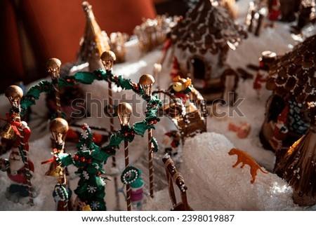 Mini street lights decirated with fir garland and wreaths around ice rink. Snowy village houses, domestic anmals. Christmas village miniature, handmade model. Made of household waste, woodchips, foam.