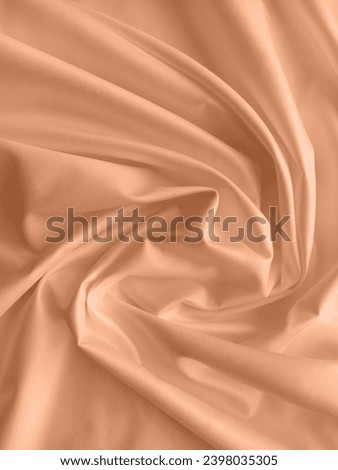 Peach fuzz is the color of the year 2024. Silk fabric folded with beautiful curves with shadows, top view