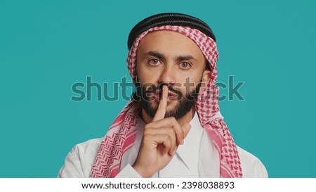 On camera, arabic person makes quiet signal with finger over lips, displaying silent mute gesture. In studio, private person does secretive confidentiality sign in an effort keep secret.