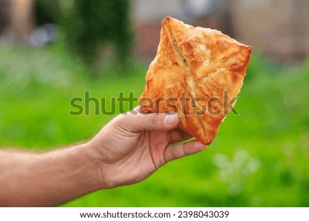 Guy's hand holds a puff pastry with cheese, snack and fast food concept. Selective focus on hands with blurred background and copy space for text. Royalty-Free Stock Photo #2398043039