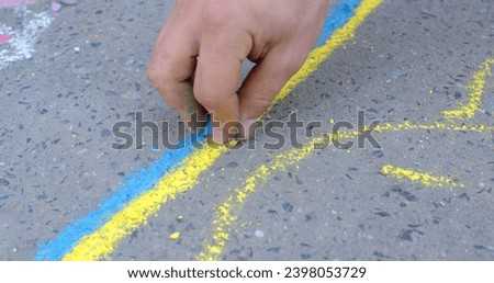 Drawings on the asphalt to decorate public spaces and add color to the urban environment, means of conveying a message or idea. Street artists hand close up, creating yellow and blue stripes.