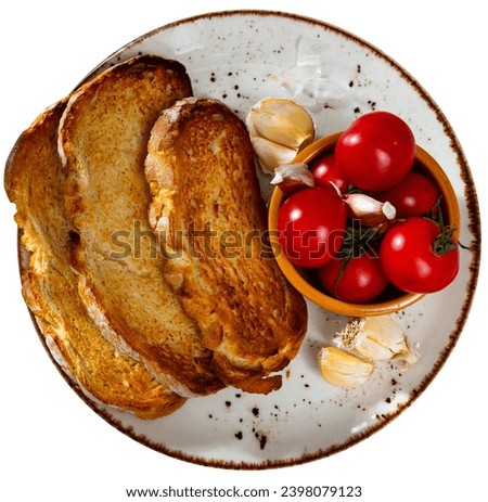 On plate are slices of toasted bread, few ripe cherry tomatoes, cloves of garlic. Spicy snack for both cool beer and wine. Isolated over white background