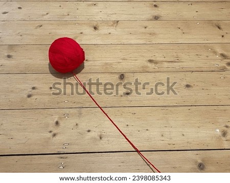 Red ball of yarn wool on timber flooring with string 