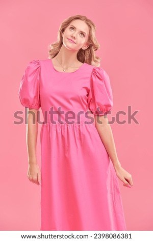 Portrait of a cute blonde girl with delicate pink makeup posing in an elegant pink dress on a pink studio background. Copy space. Hairstyles, Hollywood wave. Feminine beauty.