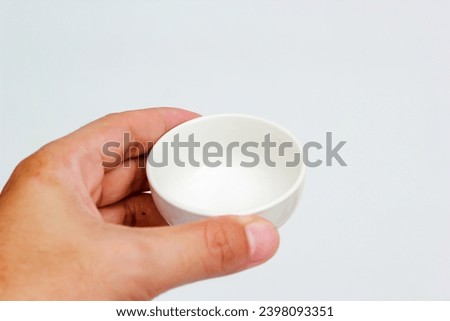 Close-up of a hand holding an empty white cup on a white background.

