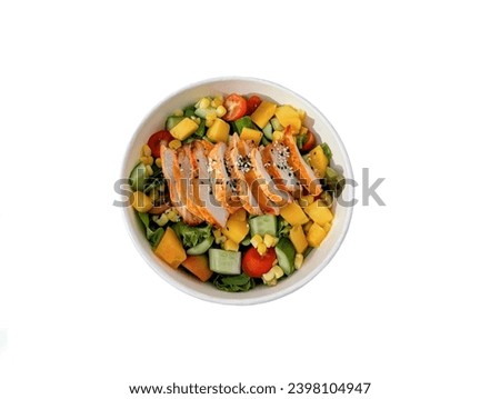 The white background in the picture is a vegetable salad in a white bowl with vegetables, cucumbers, boiled corn, boiled pumpkins. On top of the salad, there are slices of baked chicken arranged in a 