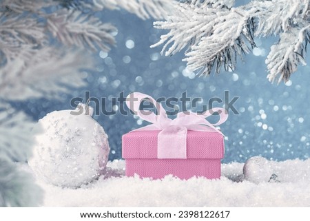 White Christmas balls and pink gift box in snow over abstract blue holiday lights
